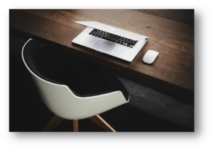 A modern workspace with a partially open silver laptop and white mouse on a dark wooden desk, paired with a sleek white chair.